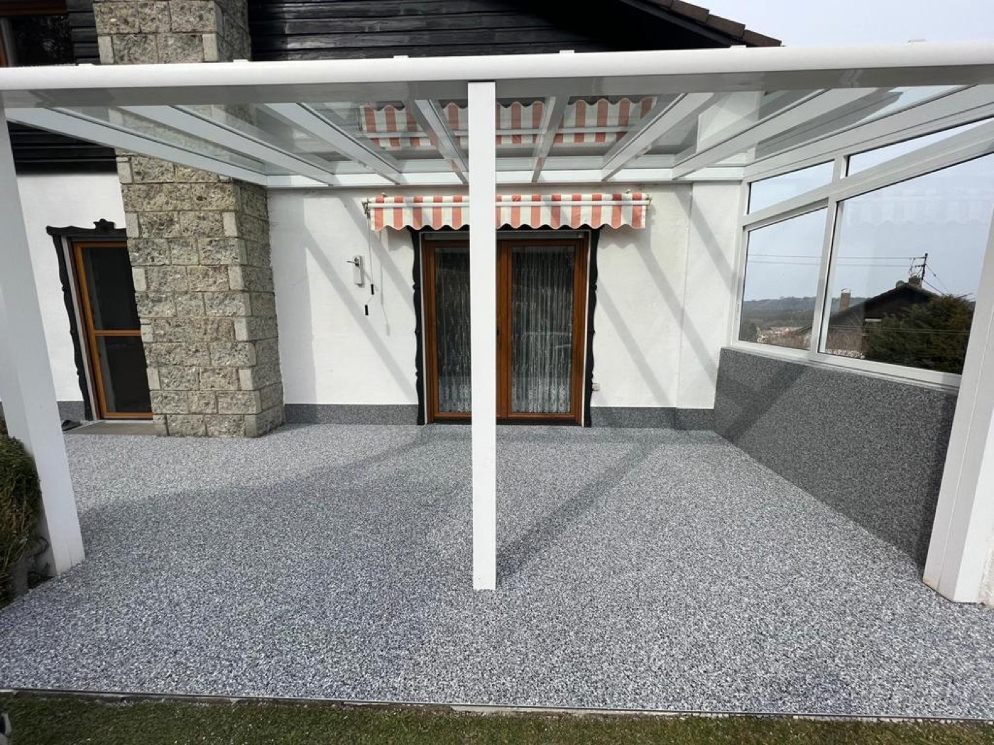 Sanierte Terrasse mit fugenlosem grauem Steinteppich unter Terrassenüberdachung